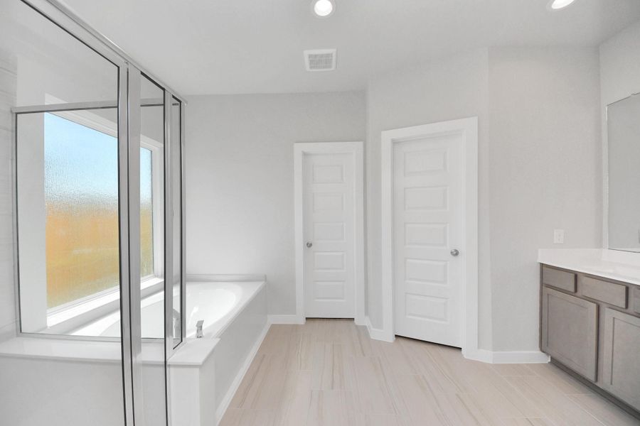 Escape to a spa-like oasis in this primary bathroom. Enjoy a walk-in shower with tile surround, a separate garden tub with custom detailing, and an elegant vanity featuring light countertops, modern hardware, and beautiful recessed lights. Experience luxury and relaxation in every detail. Sample photo of completed home with similar floor plan. Actual colors and selections may vary.