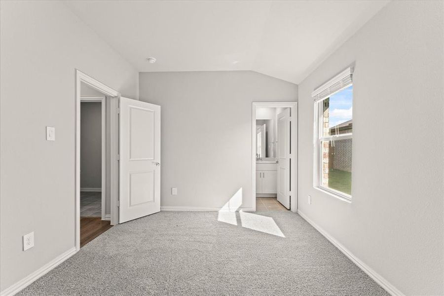 Unfurnished bedroom featuring connected bathroom, vaulted ceiling, and light colored carpet