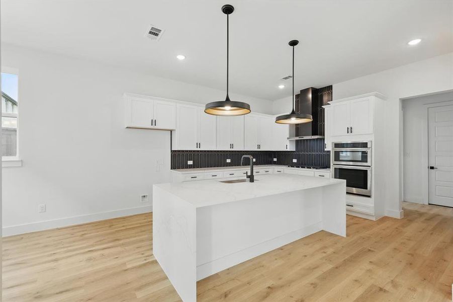 Kitchen featuring stainless steel double oven, wall chimney exhaust hood, a sink, decorative backsplash, and stovetop