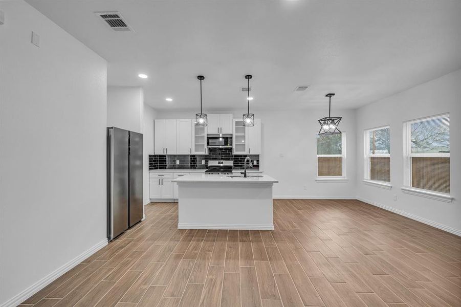 Kitchen featuring sink, decorative light fixtures, an island with sink, stainless steel appliances, and white cabinets