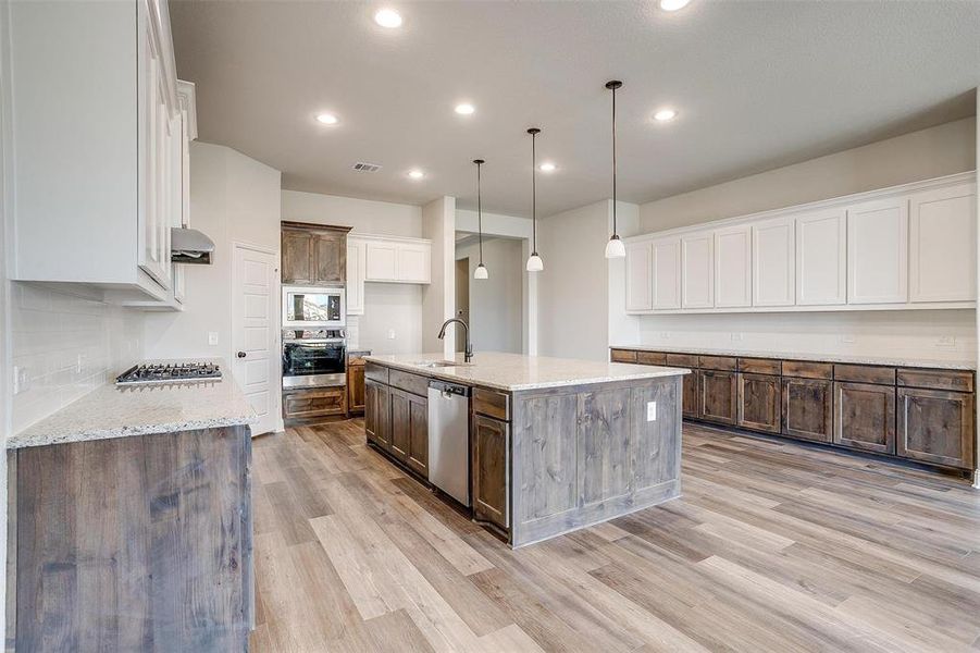 Kitchen with light wood-type flooring, an island with sink, white cabinetry, hanging light fixtures, and stainless steel appliances