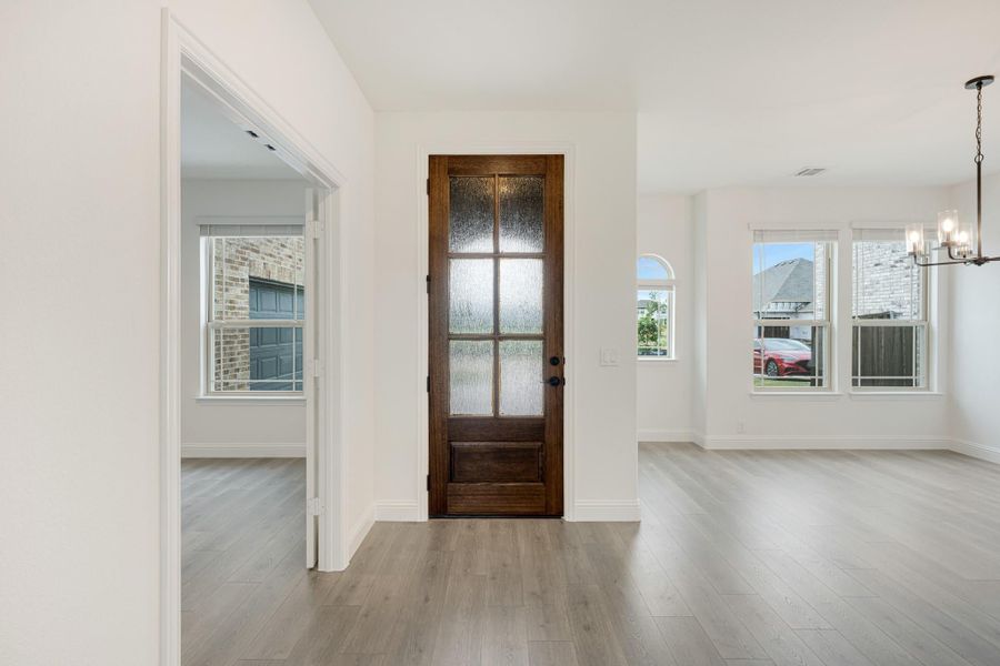 Entryway with dark wood door featuring glass panels, light hardwood floors, and chandelier in adjacent dining area