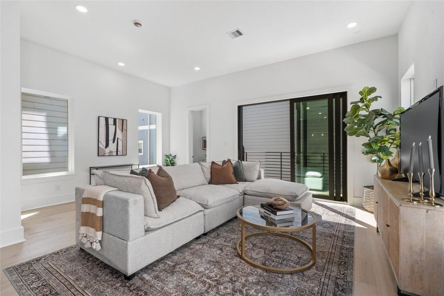 This airy living area is defined by its clean, modern design and abundant natural light. Large sliding glass doors lead to a private covered balcony, offering an easy connection to the outdoors. Wide-plank wood floors and crisp white walls contribute to a bright, open feel, while multiple windows and recessed lighting maintain a well-lit atmosphere throughout the day. The layout supports a comfortable and streamlined living experience. This airy living area is defined by its clean, modern design and abundant natural light. Large sliding glass doors lead to a private covered balcony, offering an easy connection to the outdoors. Wide-plank wood floors and crisp white walls contribute to a bright, open feel, while multiple windows and recessed lighting maintain a well-lit atmosphere throughout the day. The layout supports a comfortable and streamlined living experience.