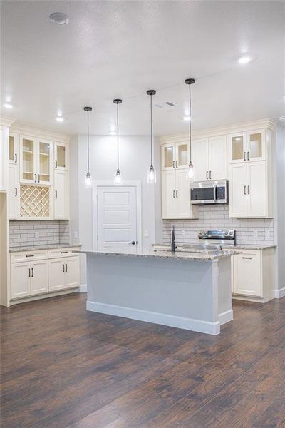 Kitchen with glass insert cabinets, backsplash, light stone counters, stainless steel microwave, and recessed lighting Kitchen with glass insert cabinets, backsplash, light stone counters, stainless steel microwave, and recessed lighting