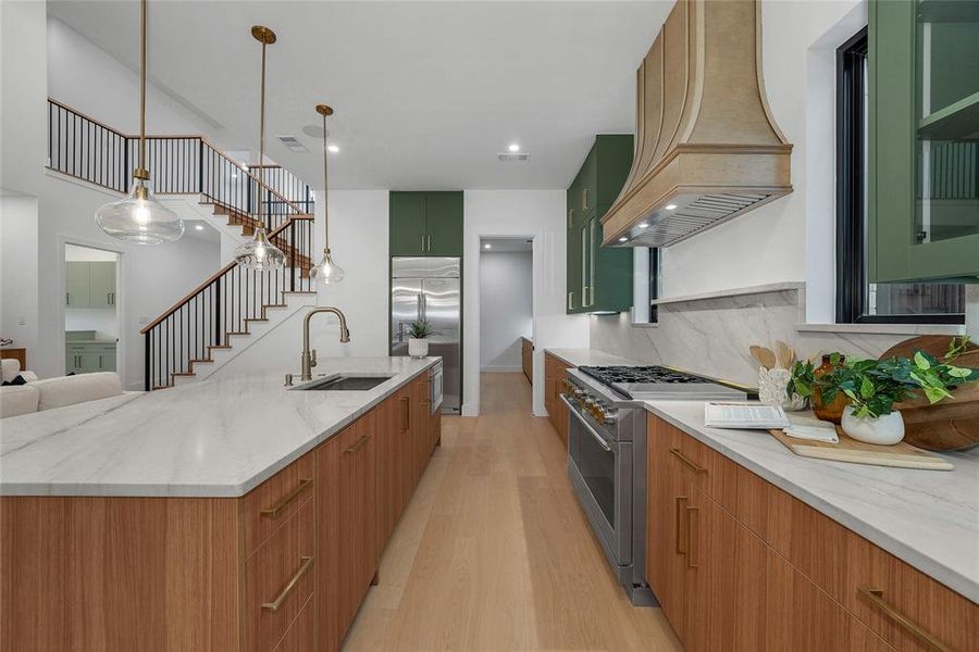 Kitchen featuring high quality appliances, light stone countertops, light wood-style floors, a large island with sink, and pendant lighting Kitchen featuring high quality appliances, light stone countertops, light wood-style floors, a large island with sink, and pendant lighting