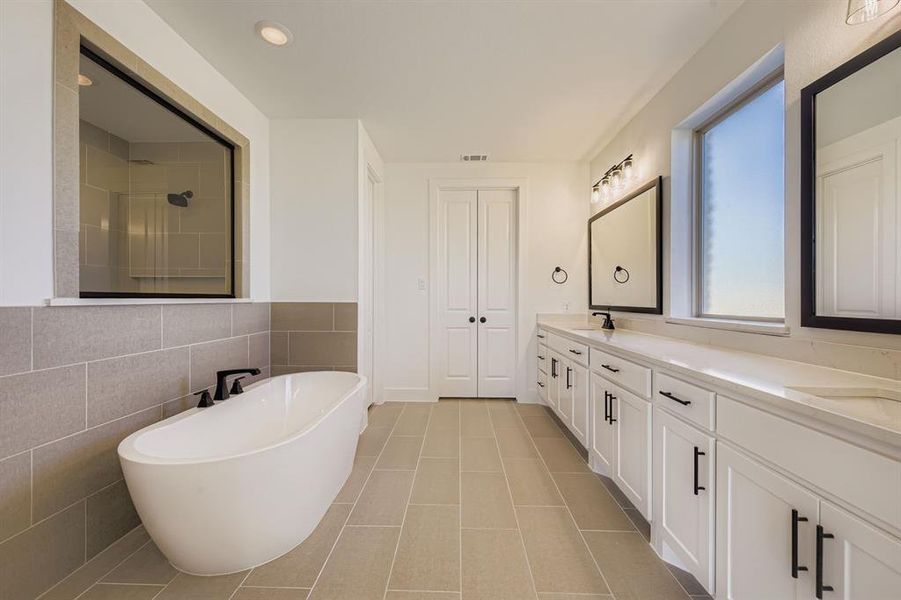 Full bathroom featuring a freestanding bath, double vanity, tile walls, a tile shower, and light tile patterned floors