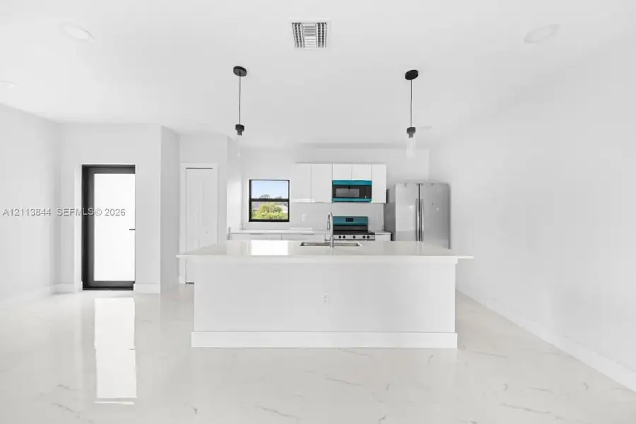 Kitchen featuring white cabinetry, a center island with a stone-finish countertop, stainless steel appliances, pendant lighting, and polished stone-finish flooring Kitchen featuring white cabinetry, a center island with a stone-finish countertop, stainless steel appliances, pendant lighting, and polished stone-finish flooring