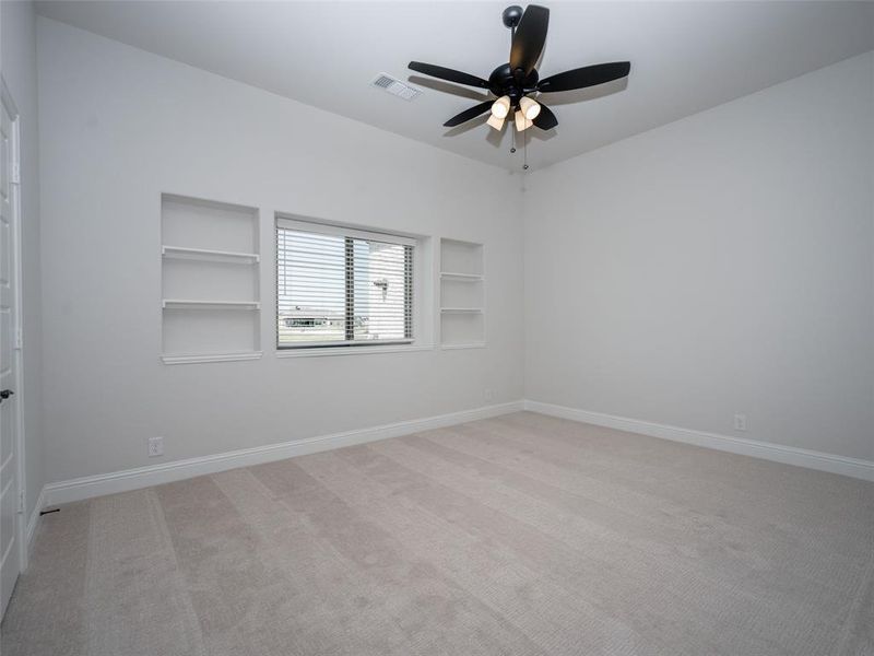 Empty room with built in shelves, light carpet, and a ceiling fan Empty room with built in shelves, light carpet, and a ceiling fan