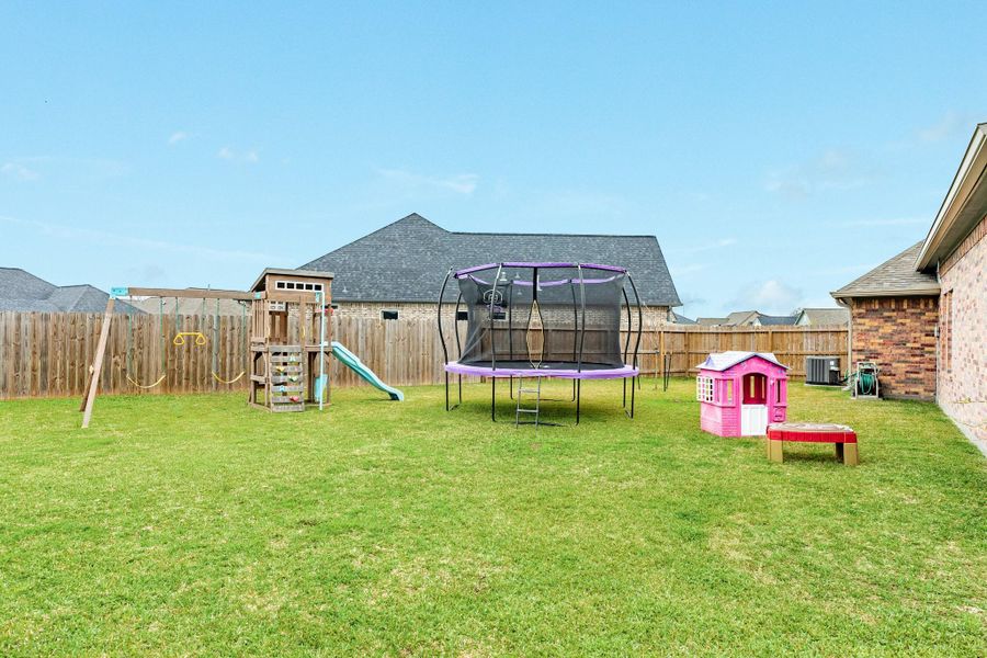 Spacious backyard with a playset, trampoline, and a small pink playhouse, perfect for family fun and relaxation. Huge cul-de-sac lot.