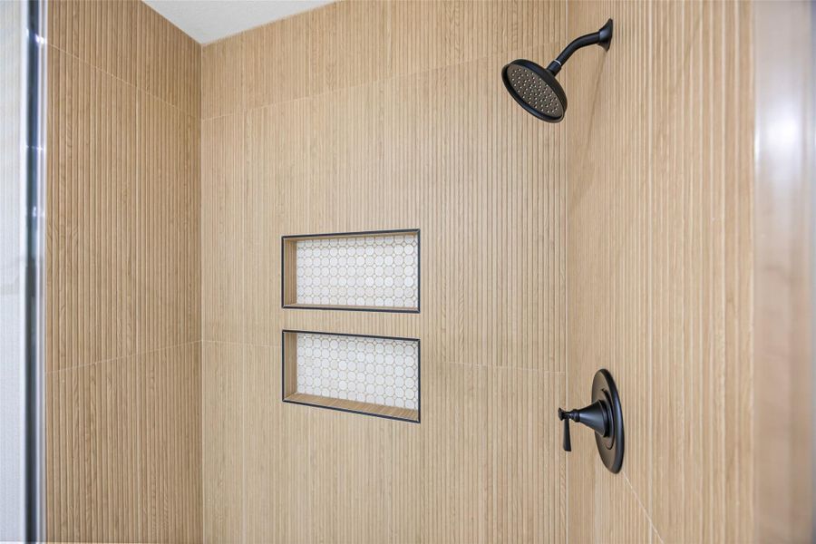 Spacious tiled shower featuring floor-to-ceiling vertical tile, dual built-in niches with mosaic accents, and matte black fixtures.