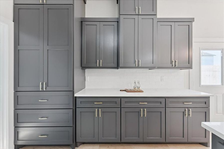 Kitchen featuring gray cabinets, light stone countertops, and decorative backsplash