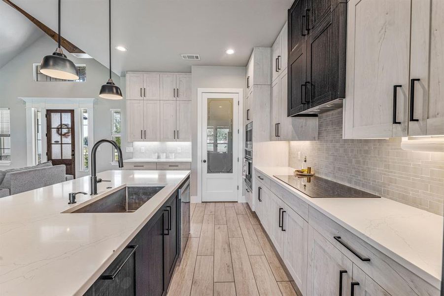 Kitchen with light stone countertops, decorative light fixtures, backsplash, lofted ceiling, and light wood-style floors