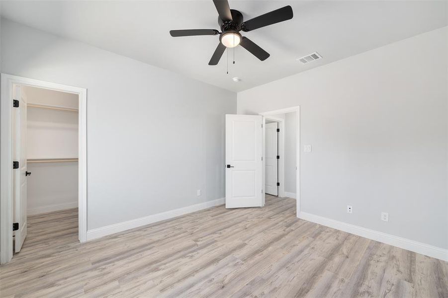 Unfurnished bedroom with a walk in closet, baseboards, light wood finished floors, and visible vents