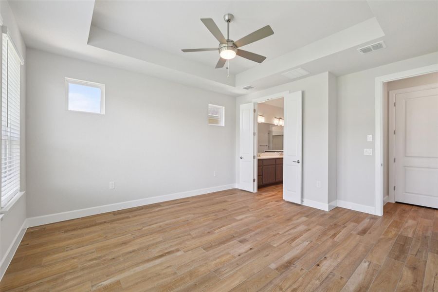Unfurnished bedroom featuring a tray ceiling, light wood-style floors, connected bathroom, and a ceiling fan