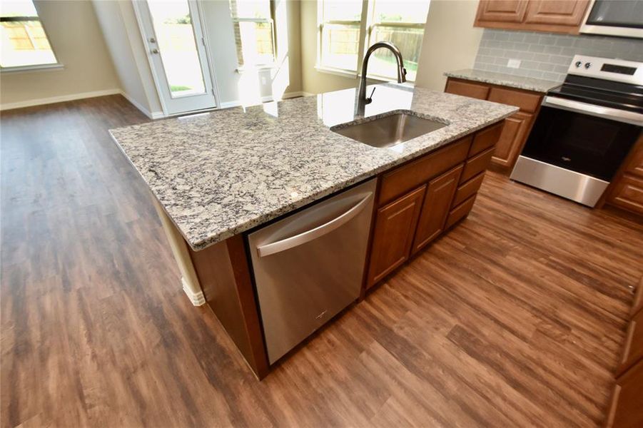 Kitchen featuring dark wood-style flooring, a kitchen island with sink, light stone counters, and open floor plan