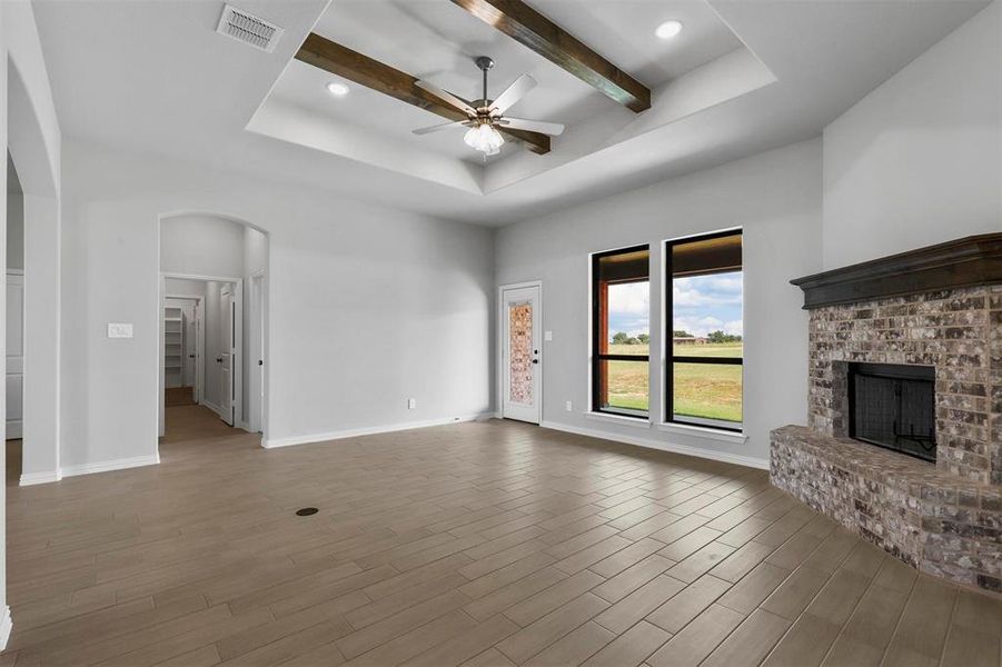 Unfurnished living room featuring hardwood / wood-style floors, a fireplace, ceiling fan, beam ceiling, and a tray ceiling