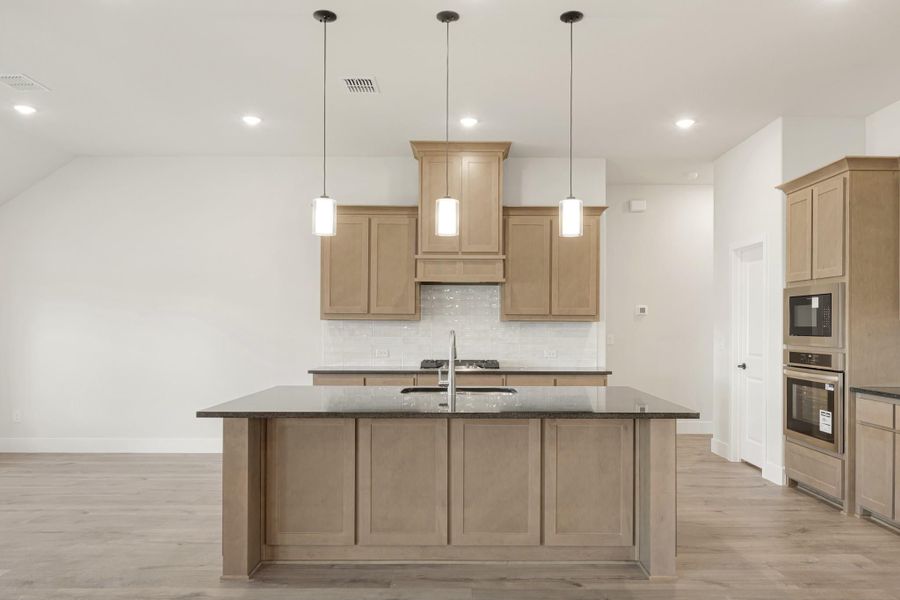 Kitchen with large island, dark granite countertops, light wood cabinets, and three pendant lights above the island.