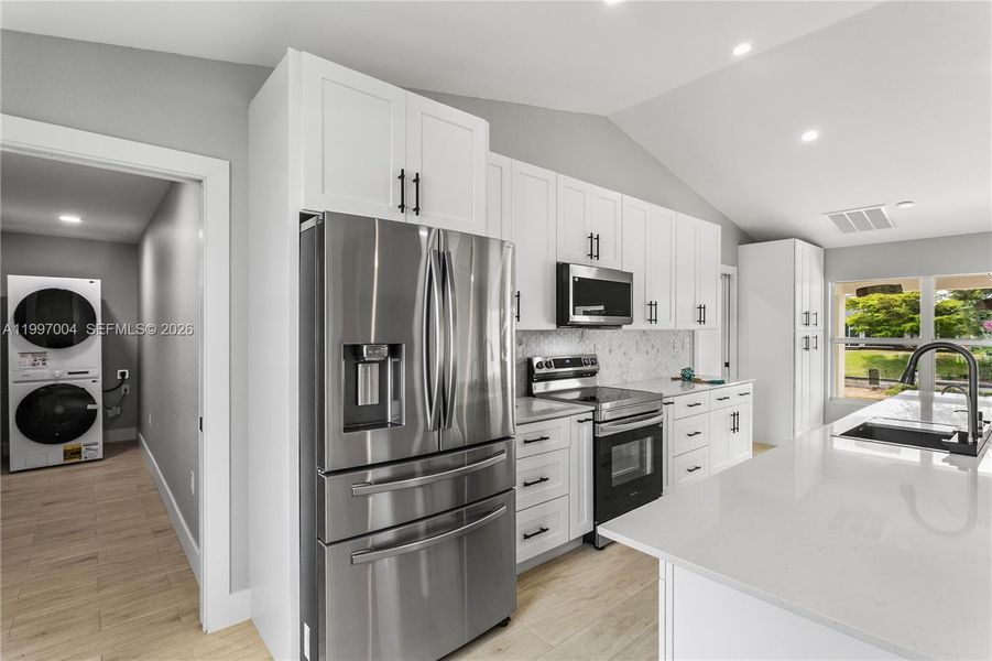 The kitchen is fully equipped with stainless steel appliances, including a French door refrigerator, smooth-top range, built-in microwave, and dishwasher, blending style with everyday functionality.