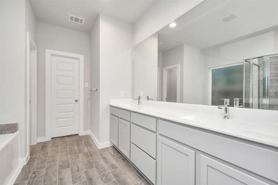 Experience luxury in this spa-like primary bathroom.  Light colored cabinets with light granite countertops, double sinks complement the space. An ideal retreat for unwinding after a long day. Sample photo of completed home with similar floor plan. As-built interior colors and selections may vary.