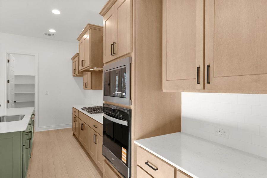 Two tone kitchen with light stone counters, oven, light wood finished floors, recessed lighting, and built in microwave