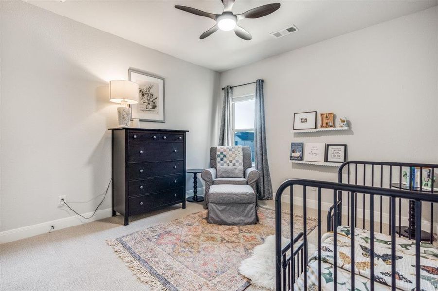 Bedroom with light colored carpet, a nursery area, and a ceiling fan