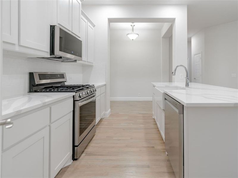 Kitchen with light stone counters, white cabinetry, a kitchen island with sink, and appliances with stainless steel finishes