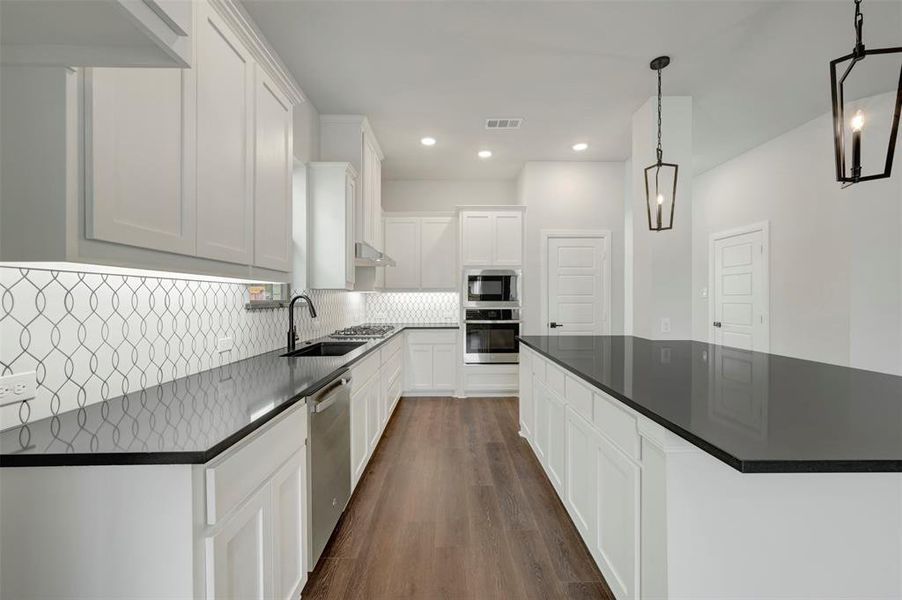 Kitchen with white cabinetry, dark wood-type flooring, stainless steel appliances, tasteful backsplash, and recessed lighting