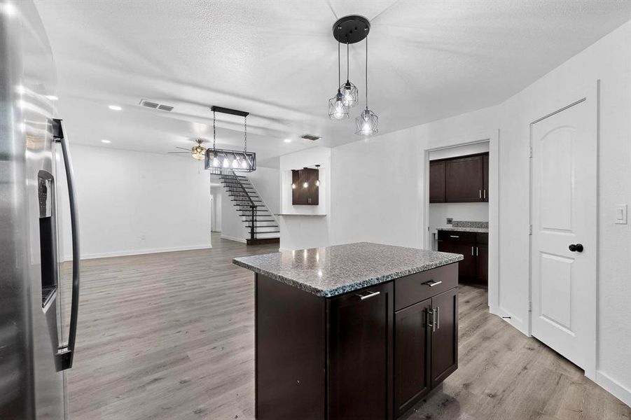 Kitchen with stainless steel fridge with ice dispenser, a center island, decorative light fixtures, dark stone counters, and dark brown cabinets
