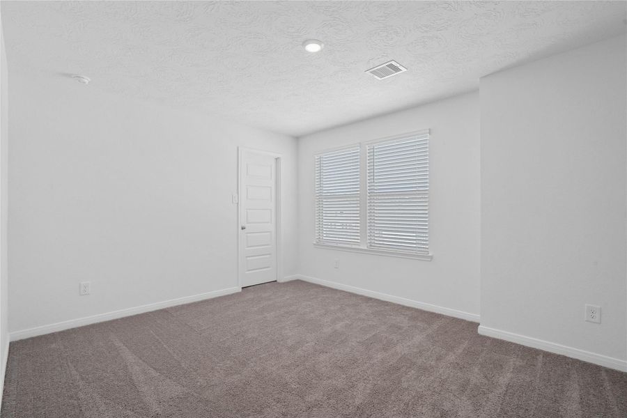 This secondary bedroom offers comfort and style with plush carpeting, neutral paint tones, recessed lighting, large windows with blinds, and a walk-in closet.