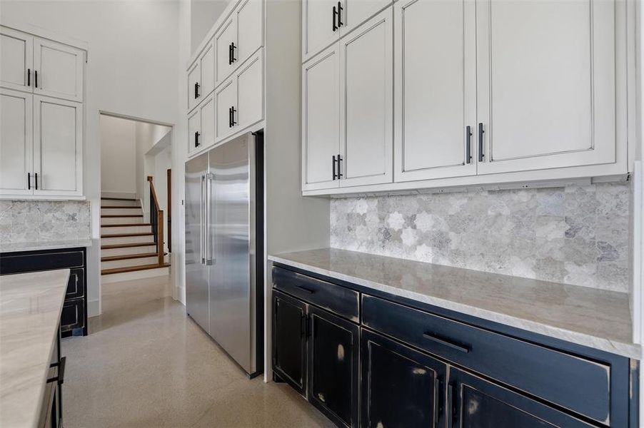 Kitchen featuring two tone cabinets, stainless steel built in fridge, tasteful backsplash, and light stone counters Kitchen featuring two tone cabinets, stainless steel built in fridge, tasteful backsplash, and light stone counters