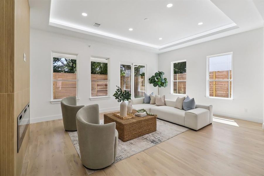 Living room with a raised ceiling, light wood-style floors, and recessed lighting