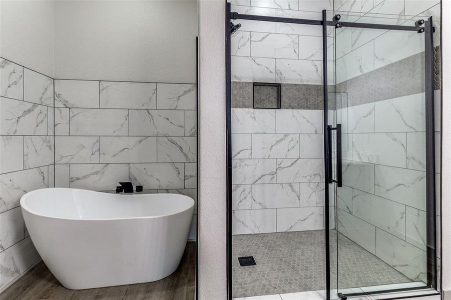Bathroom featuring a freestanding bath, tile walls, a marble finish shower, and wood finished floors Bathroom featuring a freestanding bath, tile walls, a marble finish shower, and wood finished floors