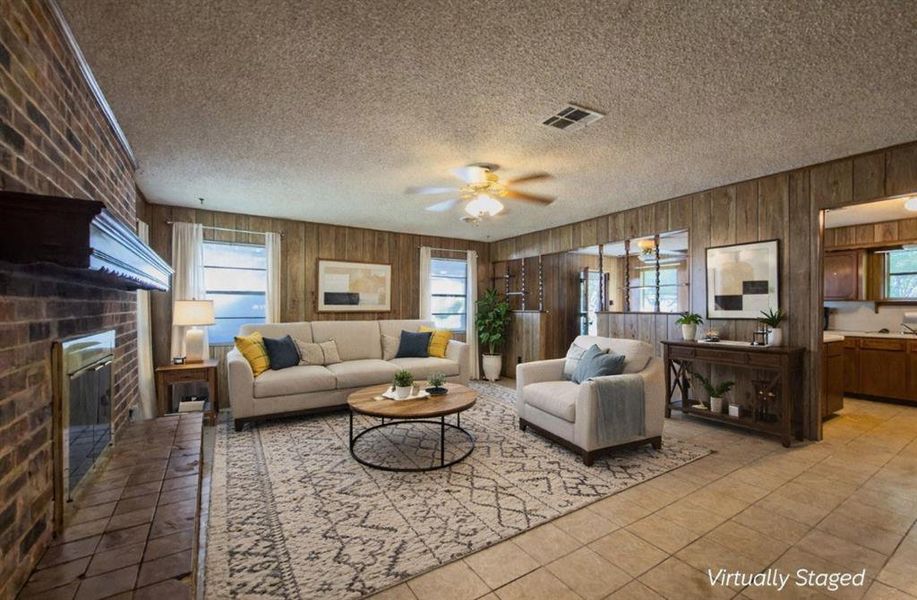 Tiled living area with healthy amount of natural light, a textured ceiling, ceiling fan, wood walls, and a brick fireplace