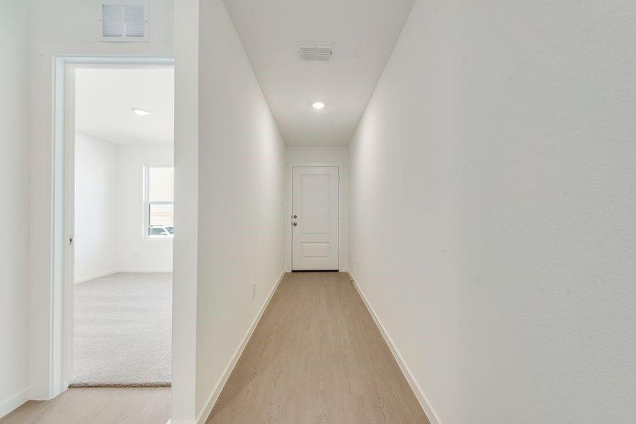 Hallway with visible vents, light wood finished floors, and baseboards