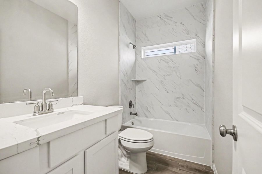 Sleek 2nd bathroom with a modern vanity, marble-style walls, and a bright tub area enhanced by natural light from a horizontal window.