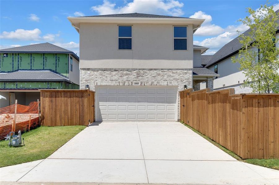 Two-story stucco and brick exterior featuring a two-car garage, concrete driveway, and wood privacy fencing