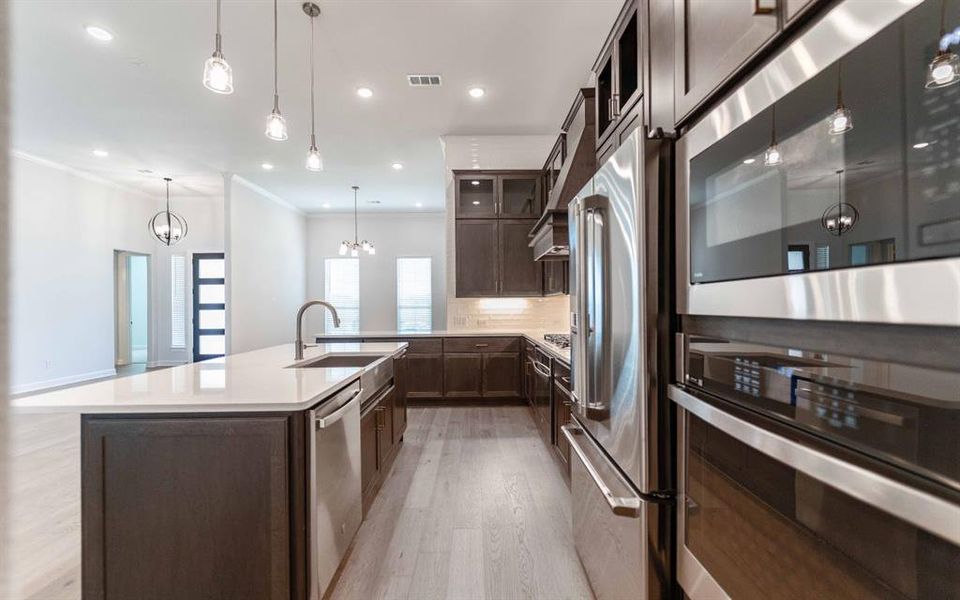 Kitchen featuring a large island with white countertop and integrated sink, stainless steel appliances, dark wood-finish cabinetry, and wood-finish flooring Kitchen featuring a large island with white countertop and integrated sink, stainless steel appliances, dark wood-finish cabinetry, and wood-finish flooring