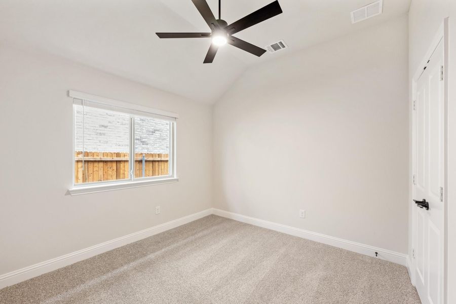 Empty bedroom with vaulted ceiling, black ceiling fan, carpet flooring, and a single window with backyard view. Empty bedroom with vaulted ceiling, black ceiling fan, carpet flooring, and a single window with backyard view.