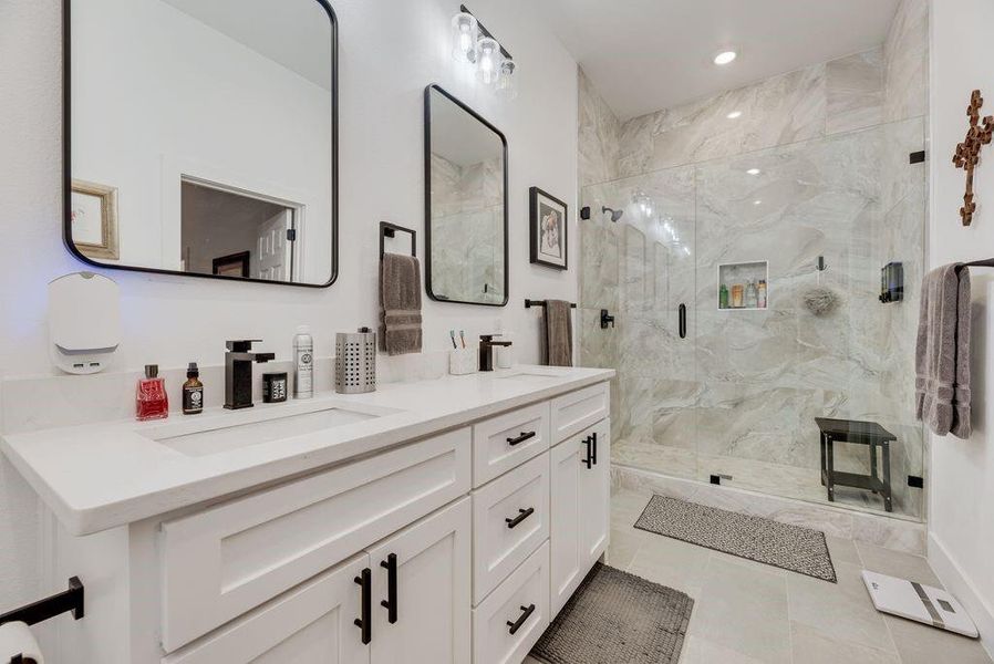 Bathroom featuring double vanity, a marble finish shower, recessed lighting, and light tile patterned floors