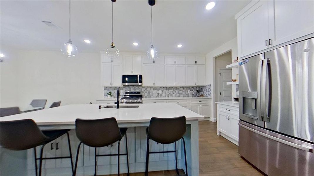 Kitchen featuring appliances with stainless steel finishes, white cabinetry, backsplash, pendant lighting, and a kitchen breakfast bar
