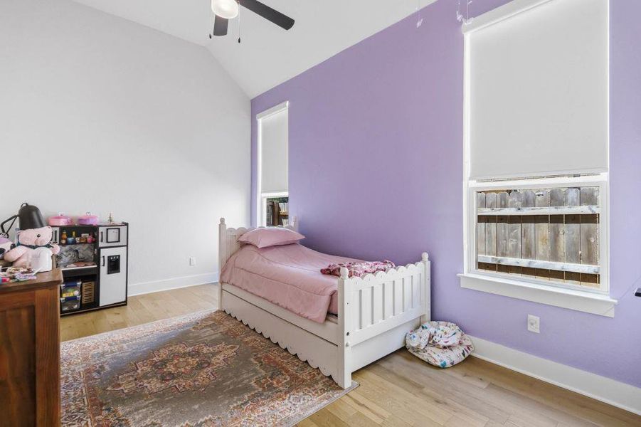 This cozy bedroom features vaulted ceilings, rich hardwood flooring, and windows with serene outdoor views.