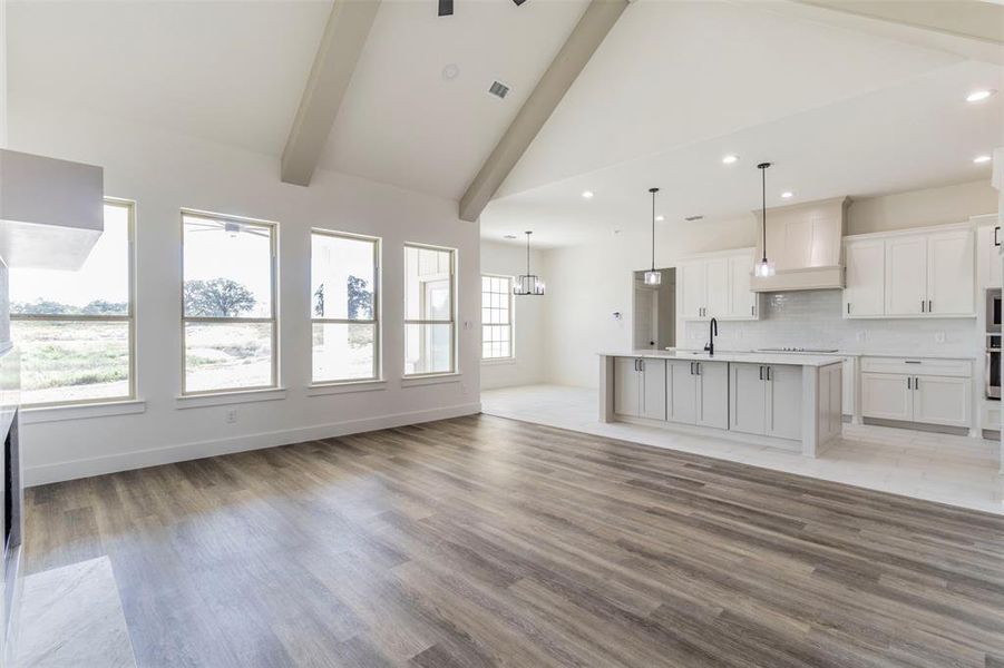 Unfurnished living room with high vaulted ceiling, light hardwood / wood-style floors, beamed ceiling, and ceiling fan with notable chandelier