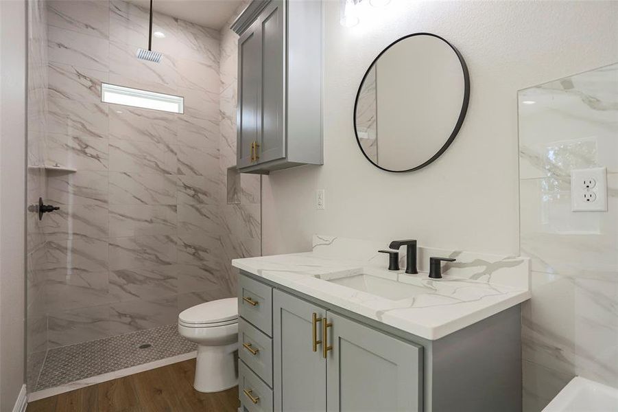 Bathroom featuring wood-type flooring, a tile shower, vanity, and toilet