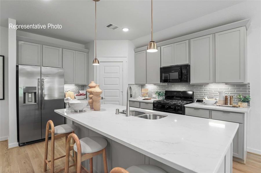 Modern kitchen featuring an island with a double basin sink, stainless steel appliances, light gray cabinetry, subway tile backsplash, and wood-finish flooring Modern kitchen featuring an island with a double basin sink, stainless steel appliances, light gray cabinetry, subway tile backsplash, and wood-finish flooring