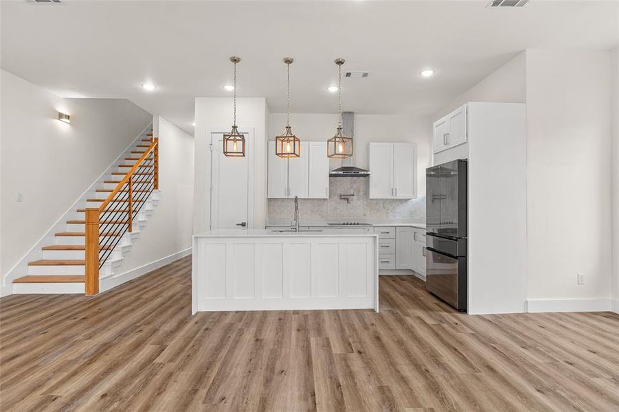 Kitchen featuring white cabinets, hanging light fixtures, a center island with sink, freestanding refrigerator, and decorative backsplash Kitchen featuring white cabinets, hanging light fixtures, a center island with sink, freestanding refrigerator, and decorative backsplash