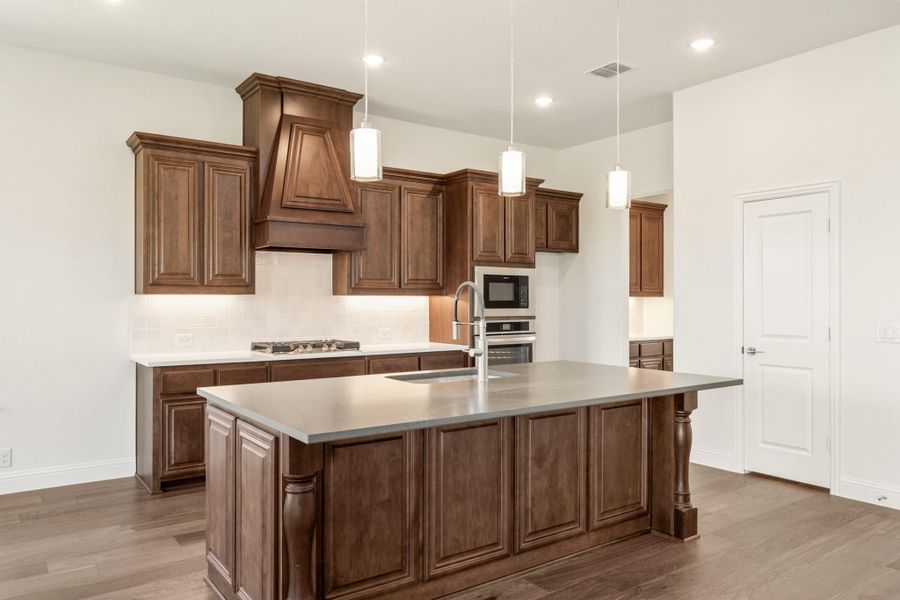 Kitchen with dark wood cabinets, large center island, pendant lights, and stainless steel appliances on hardwood floors Kitchen with dark wood cabinets, large center island, pendant lights, and stainless steel appliances on hardwood floors