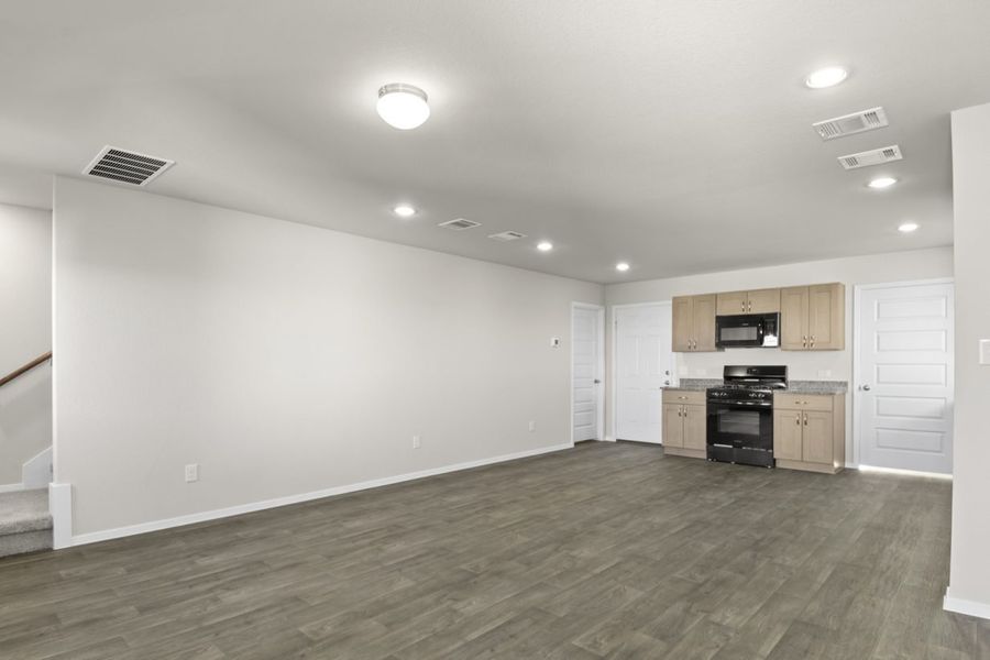 Image of a living room with dark vinyl flooring, light grey walls and and kitchen in the distance