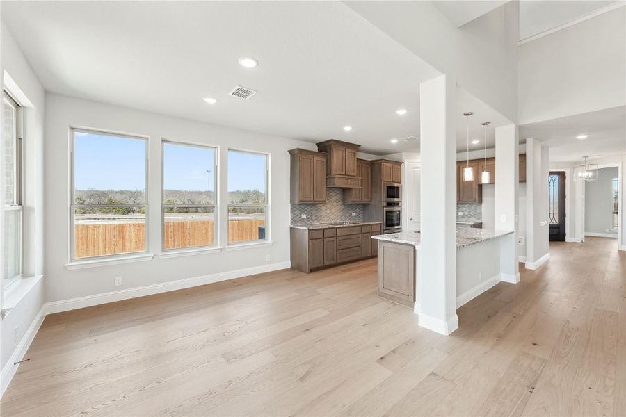 Open-plan living area with kitchen featuring brown cabinets, island, and light hardwood floors Open-plan living area with kitchen featuring brown cabinets, island, and light hardwood floors