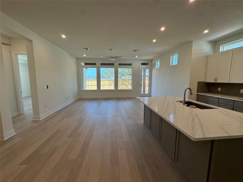 Dual tone kitchen with dual tone cabinets, light stone countertops, an island with sink, a ceiling fan, and recessed lighting