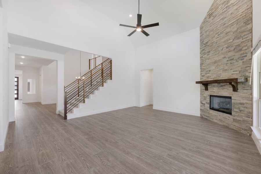 Open living room with vaulted ceiling, stone fireplace, hardwood floors, and staircase with metal railing